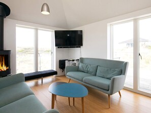 Een moderne woonkamer met een bank, een blauwe salontafel, een open haard en een aan de muur bevestigde televisie.
