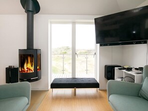 A modern living room with a wood-burning stove, a flat-screen TV, and a balcony view.