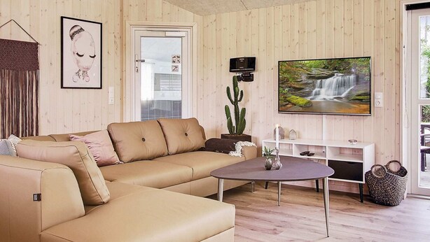 A living room with a beige sofa, a coffee table, a cactus, a TV, and a door with a glass panel. - Holiday Home in Kappeln (Kappeln)
