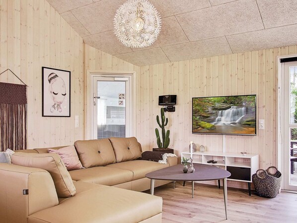 Uma sala de estar com um sofá bege, uma mesa de centro, um cacto, uma televisão e uma porta com painel de vidro.
