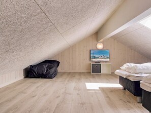 A room with a sloped ceiling, a bed, a television, and a small cabinet.