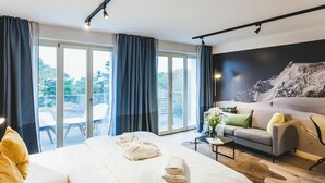 A modern hotel room with a large bed, a sofa, a coffee table, and a balcony with a view of greenery. - Beautiful apartment for 2 people with WIFI, pool, TV, terrace and pets allowed (Sassnitz)