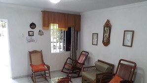 Una sala de estar con una mesa de centro de vidrio, dos sillas de madera, un sofá y una ventana con cortina.