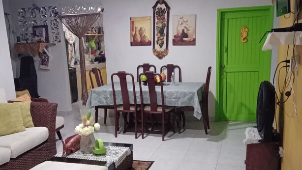 Una sala de estar con un sofá, una mesa de centro con adornos, un comedor con mesa y sillas, y una puerta verde.