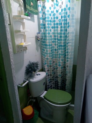 A small bathroom with a toilet, a shelf with toiletries, and a shower curtain with a polka dot pattern.