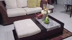 Sala de estar com um sofá marrom, almofadas brancas, uma mesa de centro com um jogo americano de renda e um vaso com flores.