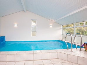 An indoor swimming pool with clear blue water, a tiled floor, and metal pool ladders.