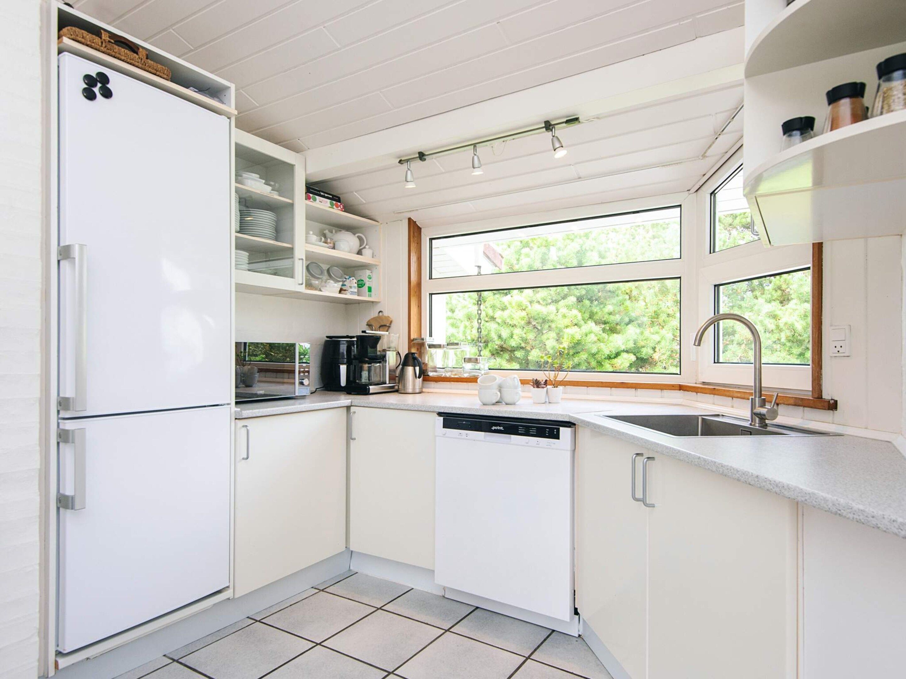 Een moderne keuken met witte kasten, een inbouwvaatwasser, een koffiezetapparaat en een raam met uitzicht op groen.