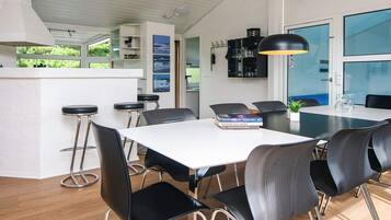 Eine moderne Küche mit weißen Schränken, einer zentralen Kochinsel mit Sitzgelegenheiten und einem Essbereich mit weißem Tisch und schwarzen Stühlen.