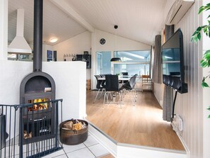 A modern interior with a fireplace, dining area, and a TV mounted on the wall. - 4 Star Holiday Home in Vejers Strand (Vejers Strand)