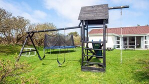 Een speeltuin met schommels en een klimrek in een gazon, met een huis op de achtergrond.