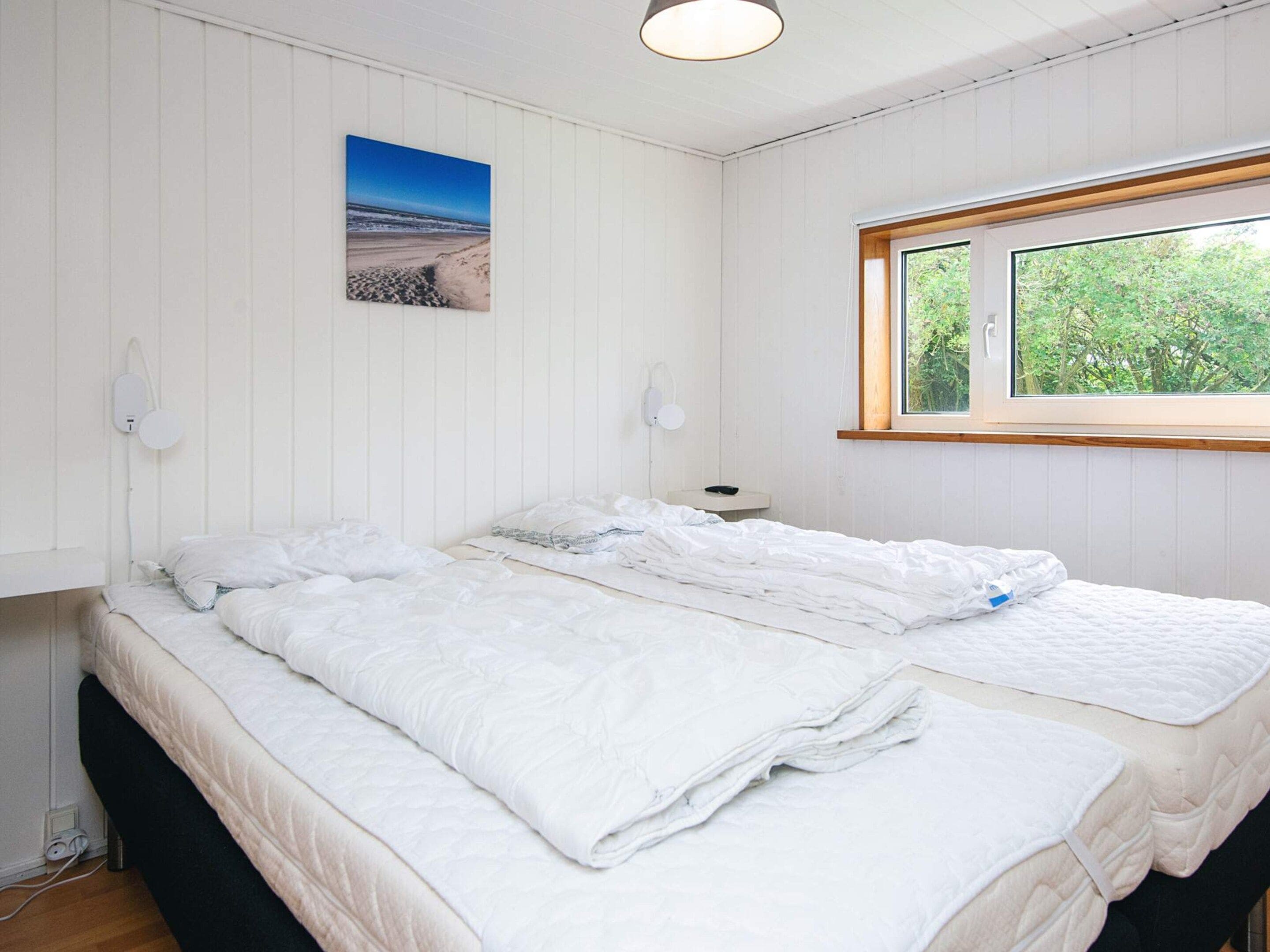 A bedroom with a bed, a window, and a wall-mounted picture.