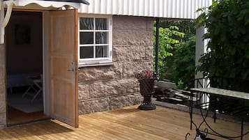 A wooden deck with a table and chairs, a cat, and a door leading to a room.