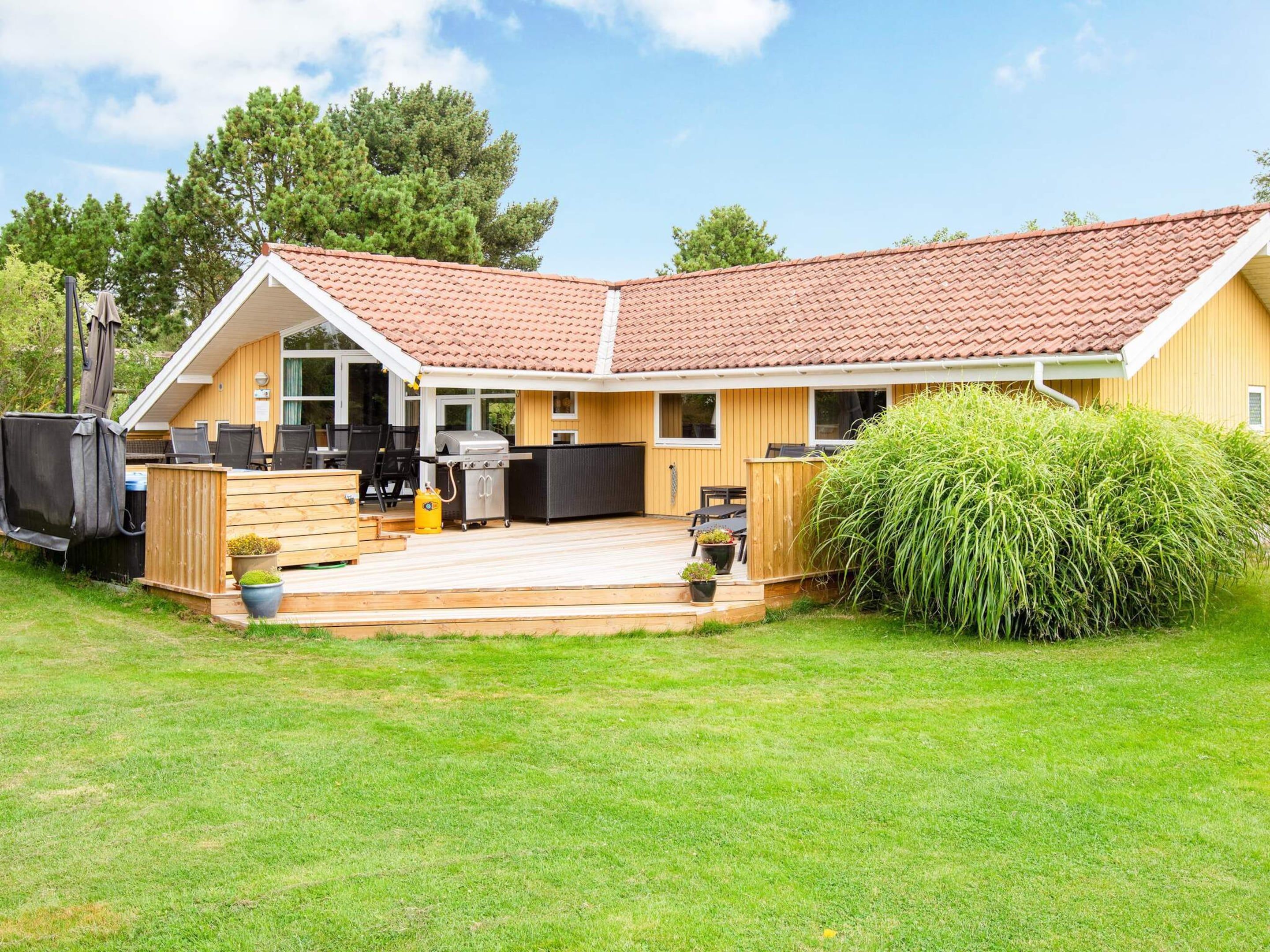 Ein zweistöckiges Haus mit Terrasse, Sitzgelegenheit im Freien und Grill.
