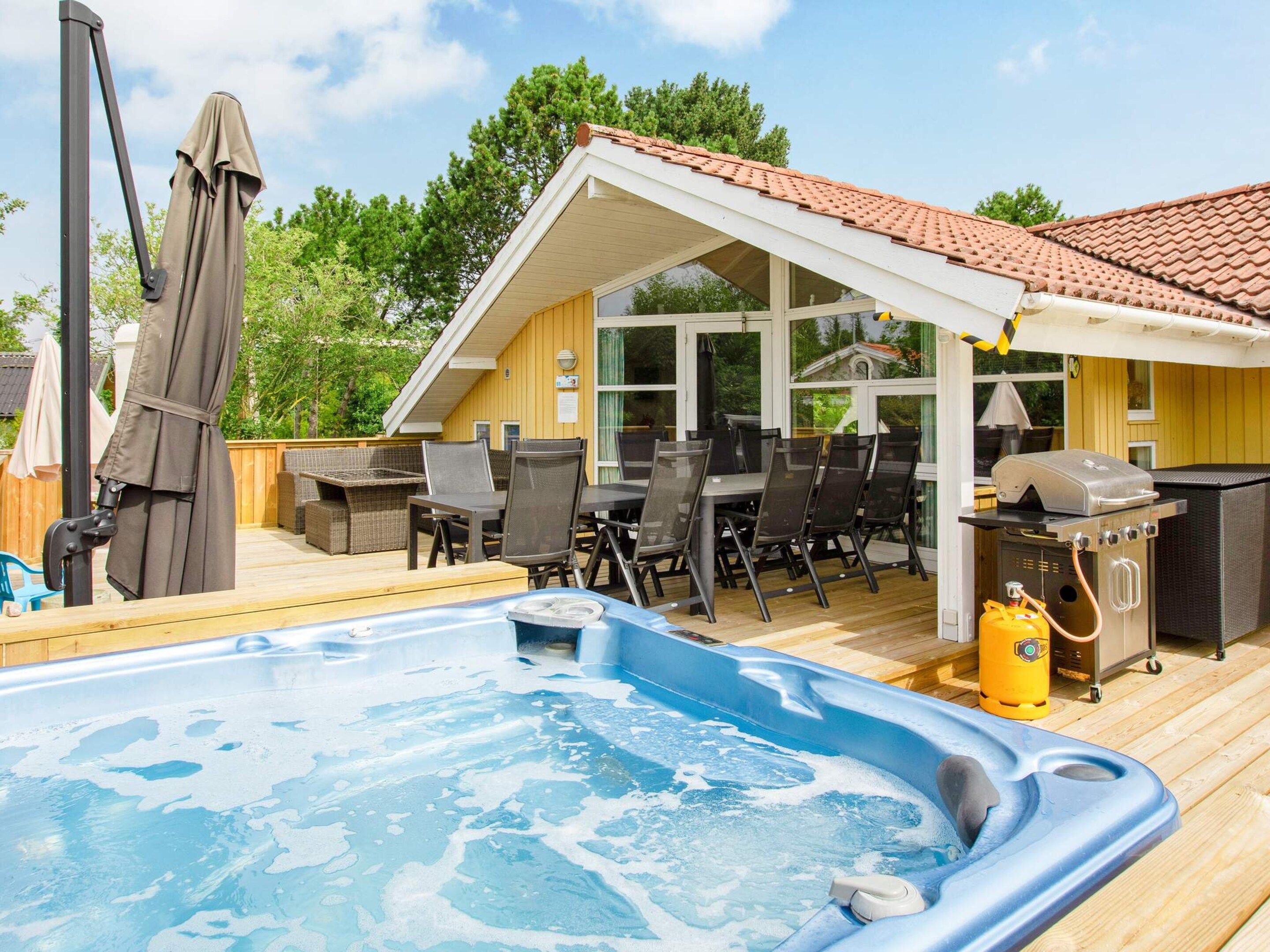 Un jacuzzi en una terraza de madera, un porche cubierto con mobiliario exterior y una parrilla.