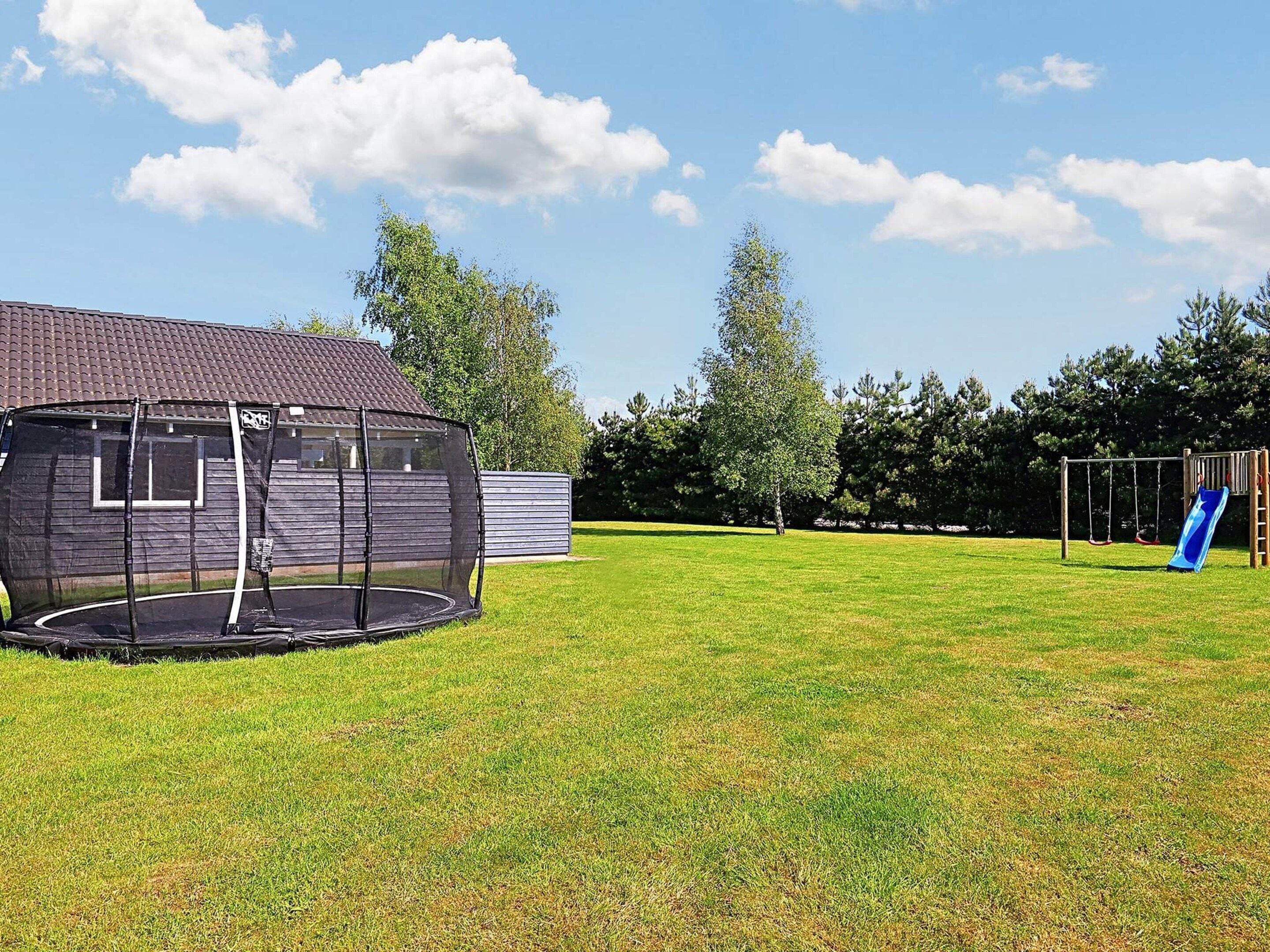 A backyard with a trampoline, a swing set, and a slide.