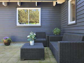 Une terrasse avec des meubles en osier, une plante en pot et une fenêtre donnant sur des arbres.