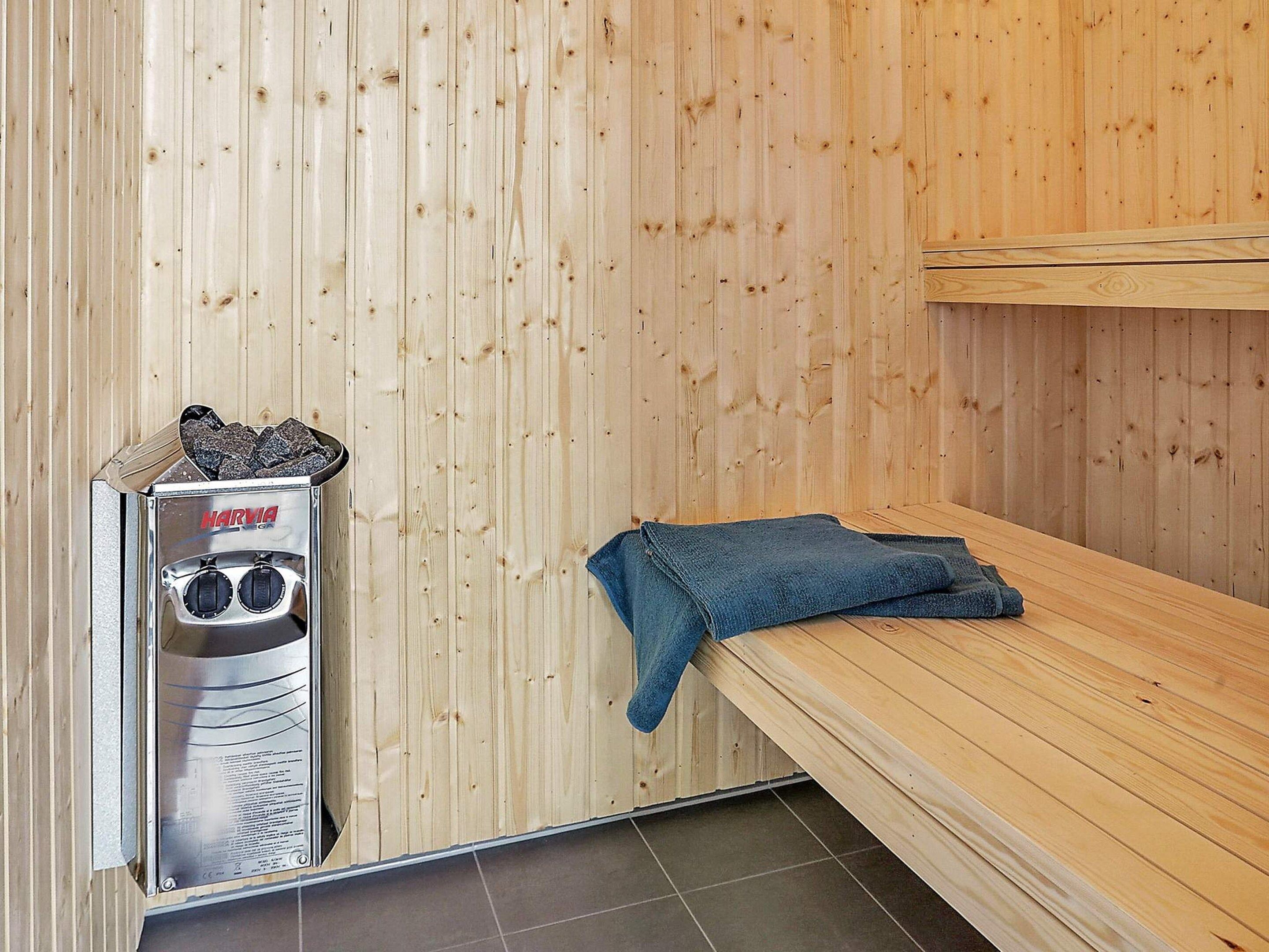 A sauna room with a Harvia sauna machine, a bench, and a folded towel.