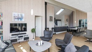A modern living room with a flat-screen TV, leather sofas, a coffee table, and a dining area with a long table and chairs. - Luxury Holiday Home in Falster near Sea (Vaeggerlose)