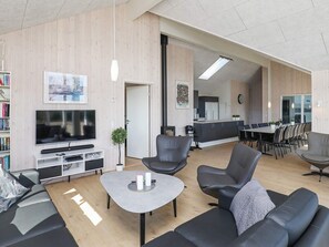 A modern living room with a flat-screen TV, leather sofas, a coffee table, and a dining area with a long table and chairs. - Luxury Holiday Home in Falster near Sea (Vaeggerlose)