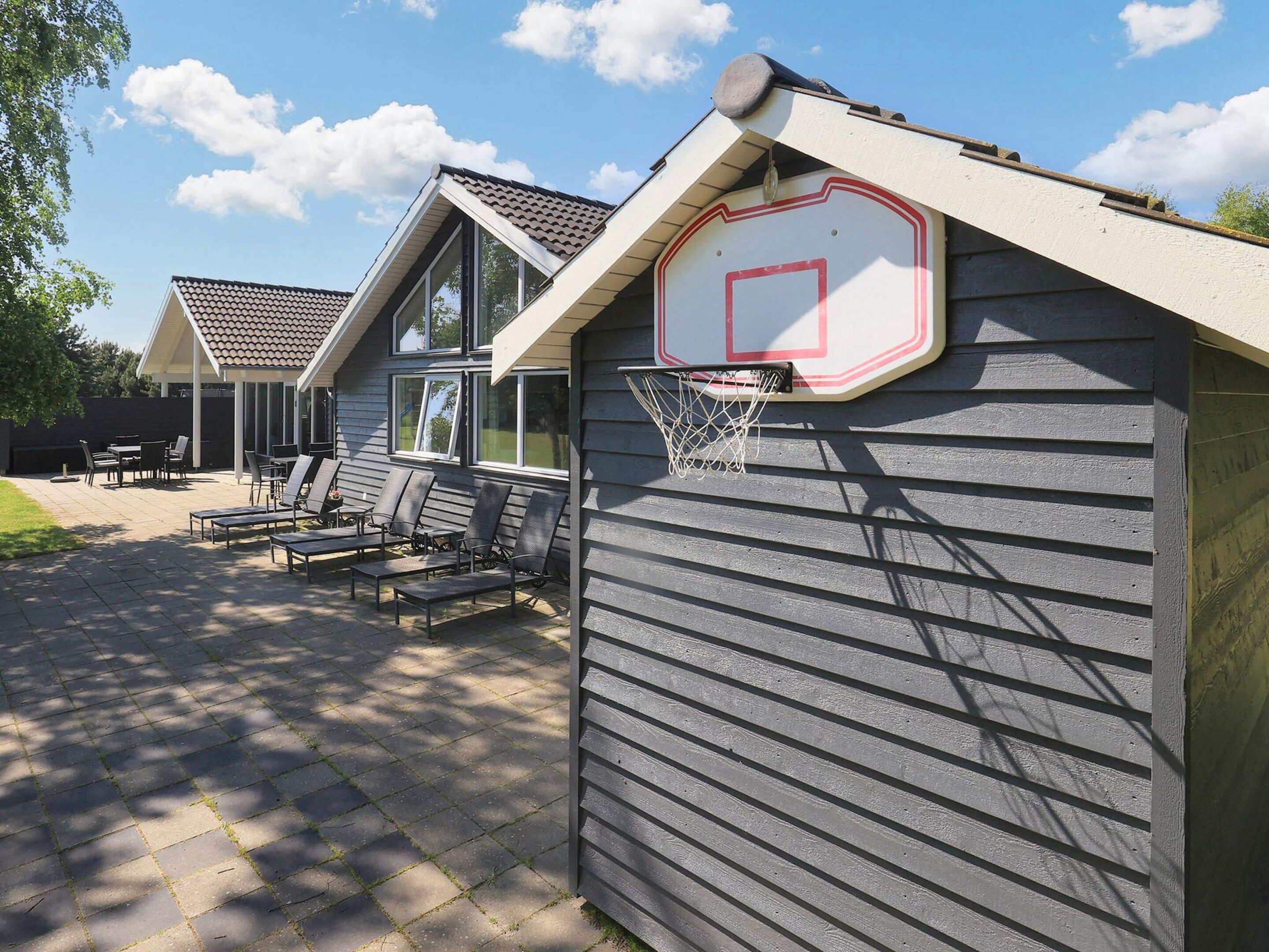 A residential area with a basketball hoop attached to a house, outdoor seating, and a patio.