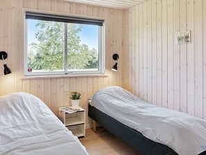 Une chambre avec deux lits simples, une fenêtre, une petite table avec une plante et un tableau accroché au mur.