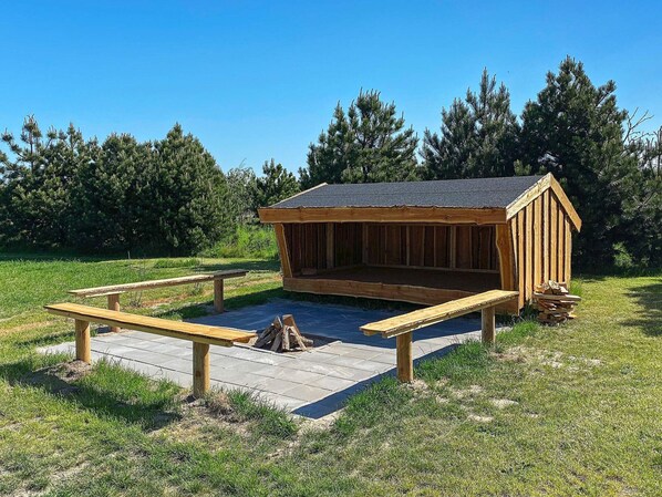 A wooden cabin with a sloped roof, surrounded by a grassy area with two picnic tables. - Luxury Holiday Home in Falster near Sea (Vaeggerlose)