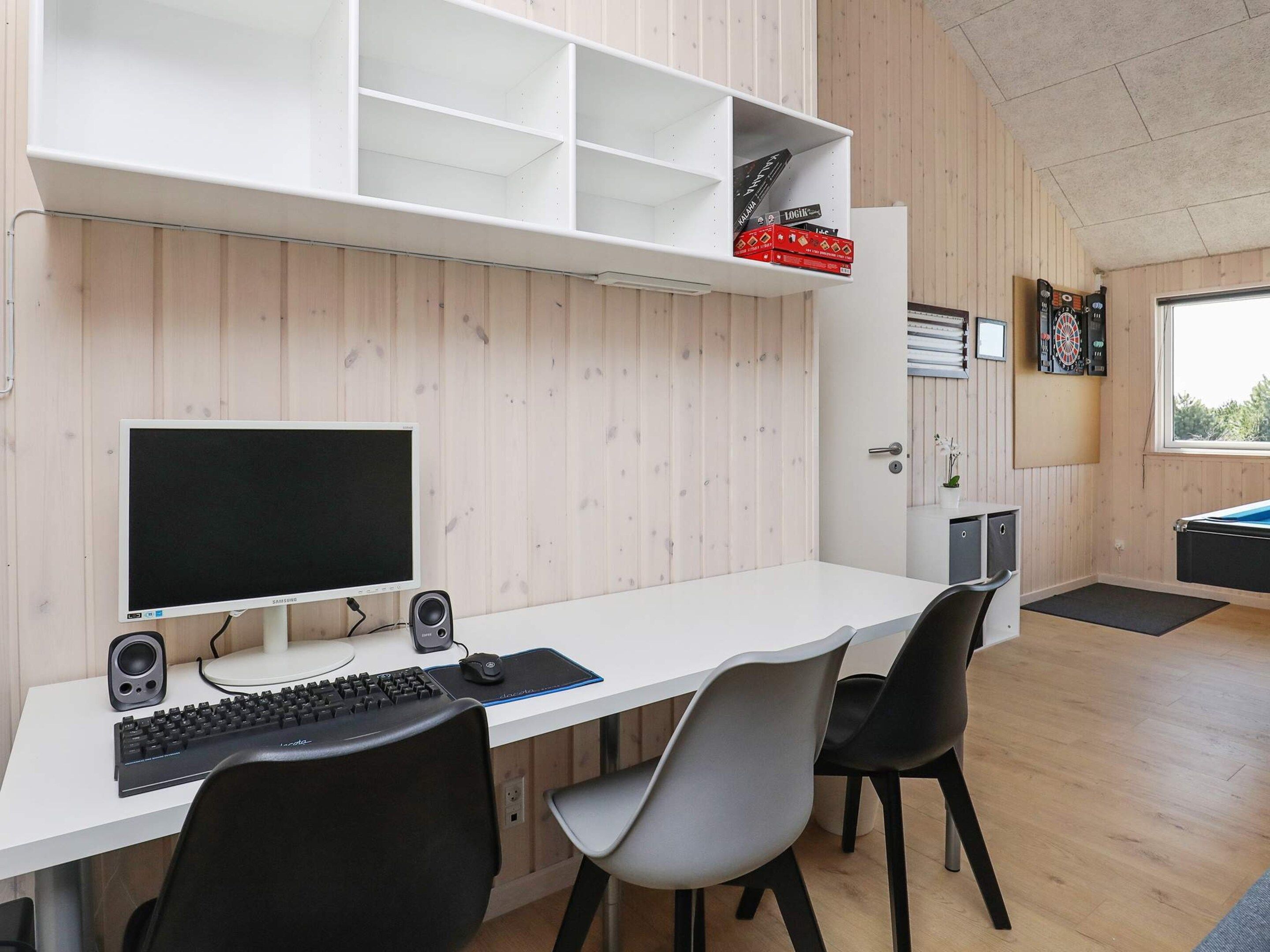 A modern room with a white desk, black and grey chairs, a computer setup, and a dartboard.