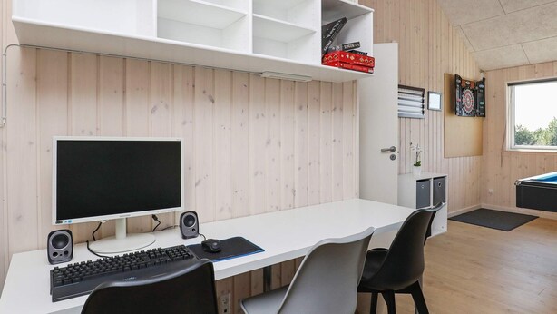 A modern room with a white desk, black and grey chairs, a computer setup, and a dartboard. - Luxury Holiday Home in Falster near Sea (Vaeggerlose)