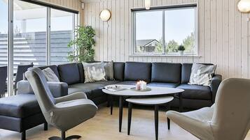 A modern living room with a sectional sofa, two armchairs, a round coffee table, and a potted plant.