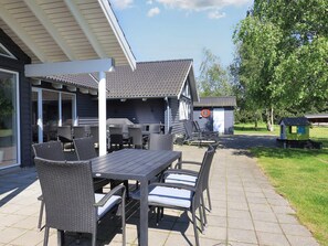 An outdoor patio with a table and chairs, a covered seating area, and a small shed with a clock. - Luxury Holiday Home in Falster near Sea (Vaeggerlose)