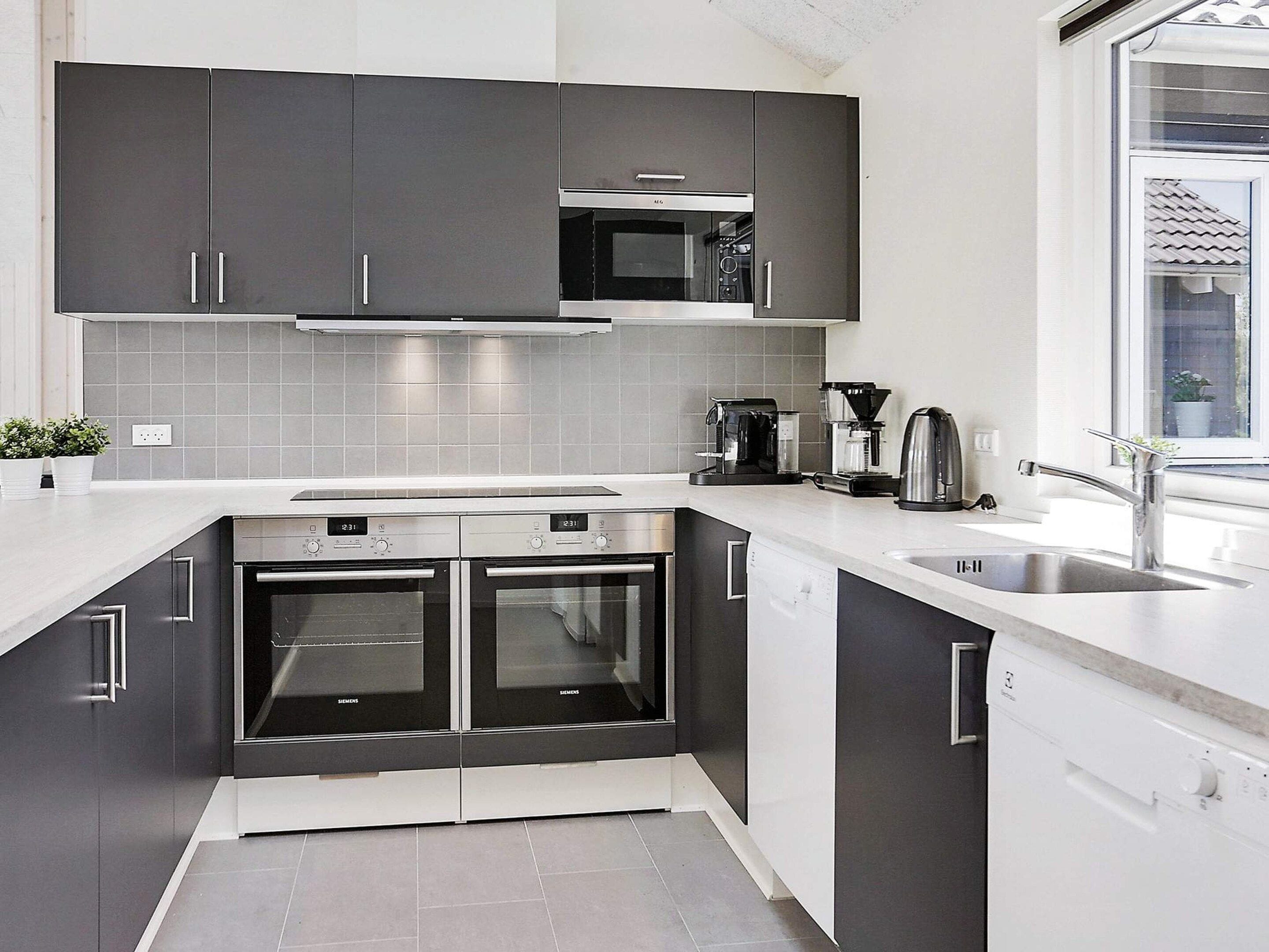 Cozinha moderna com armários escuros, forno duplo, cafeteira e janela com vista.