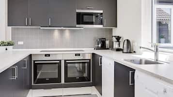 Cozinha moderna com armários escuros, forno duplo, cafeteira e janela com vista.