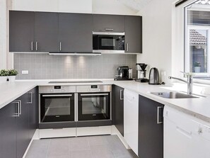 Una cocina moderna con armarios oscuros, un horno doble, una cafetera y un ventanal con vistas.
