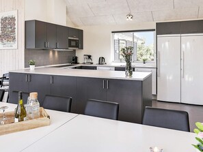 Et moderne køkken med mørke skabe, en central ø og et hvidt køleskab.