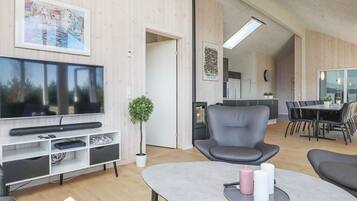 Uma sala de estar moderna com televisão de tela plana, área de estar, mesa de jantar e cozinha ao fundo.
