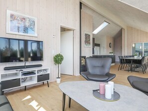 En moderne stue med et fladskærms TV, siddepladser, et spisebord og et køkken i baggrunden.