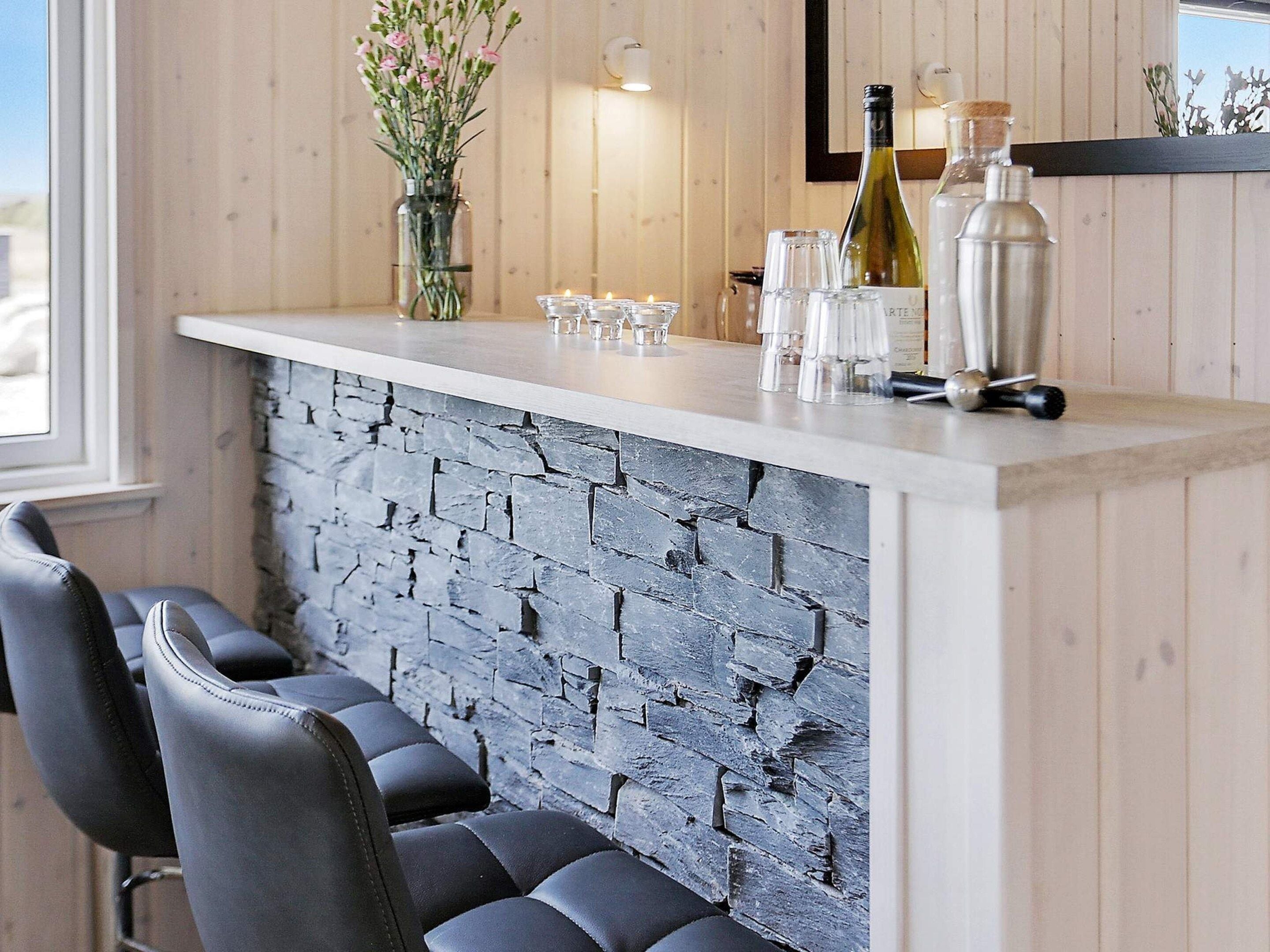 A bar area with a stone wall, bar stools, and a wine bottle.