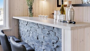 A bar area with a stone wall, bar stools, and a wine bottle. - Luxury Holiday Home in Falster near Sea (Vaeggerlose)