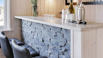 A bar area with a stone wall, bar stools, and a wine bottle.