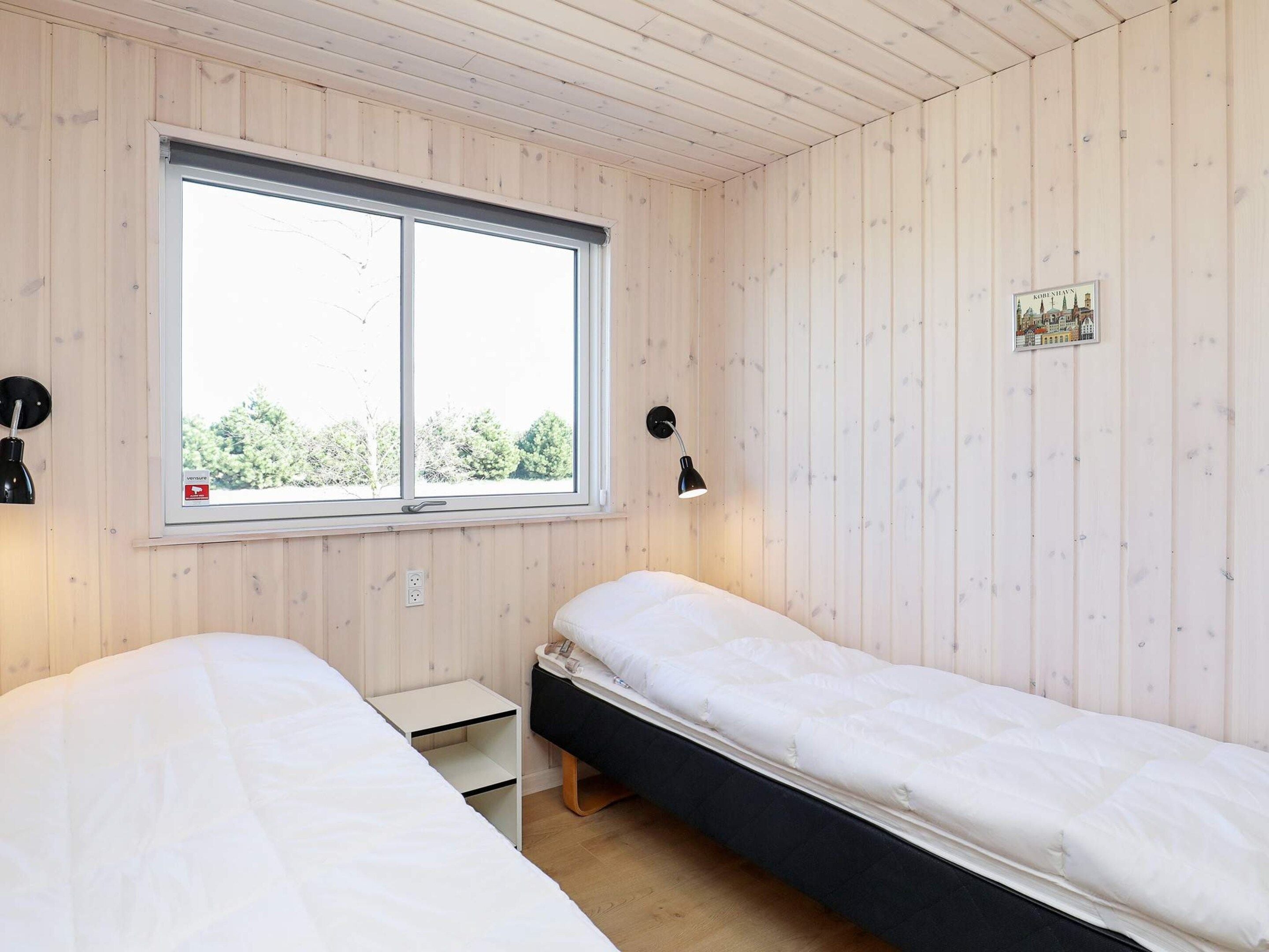 A room with two beds, a window, a wall-mounted lamp, and a small picture frame.