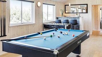 A pool table with balls, a foosball table, and a billiard cue rack.