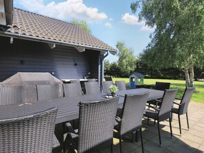 An outdoor dining area with a covered grill, wicker furniture, and a small playhouse in the background. - Luxury Holiday Home in Falster near Sea (Vaeggerlose)