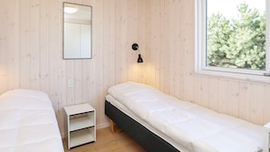 A room with two beds, a small white nightstand, a wall-mounted mirror, a window with a view of trees, and a wall-mounted lamp. - Luxury Holiday Home in Falster near Sea (Vaeggerlose)