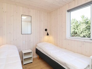A room with two beds, a small white nightstand, a wall-mounted mirror, a window with a view of trees, and a wall-mounted lamp. - Luxury Holiday Home in Falster near Sea (Vaeggerlose)