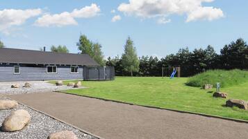 A building with a grey exterior, a paved driveway, and a playground with a slide.