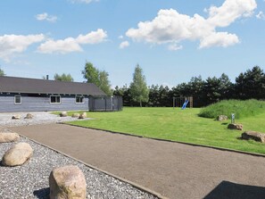 A building with a grey exterior, a paved driveway, and a playground with a slide. - Luxury Holiday Home in Falster near Sea (Vaeggerlose)