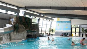 Une piscine intérieure dotée d’un toboggan aquatique, d’un espace détente et d’une fresque représentant une scène de plage.