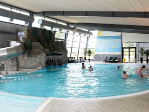 En inomhuspool med en vattenrutschkana, en sittgrupp och en väggmålning som föreställer en strandscen.