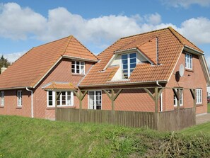 A two-story brick house with a sloped roof, wooden beams, and a fenced yard.